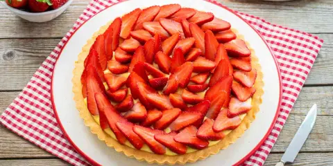 Deliziosa crostata di fragole con crema pasticcera, decorata con fragole fresche affettate. Un dolce estivo perfetto.