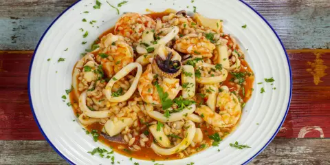 Un invitante risotto alla pescatora, ricco di gamberi, calamari e cozze, guarnito con prezzemolo fresco.