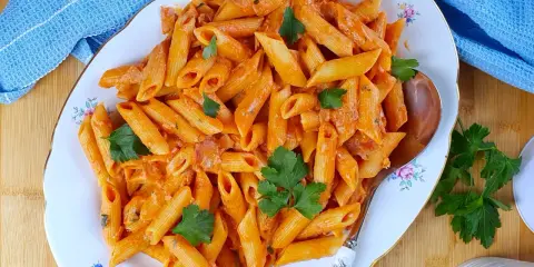 Penne al baffo cremose e saporite, guarnite con prezzemolo fresco, servite su un piatto elegante.