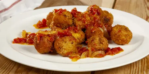 Polpette di pesce dorate e saporite, condite con un sugo rosso di pomodoro e cipolla, servite su un piatto bianco.