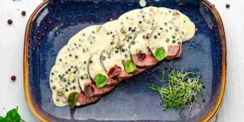 Fette affettate in salsa cremosa al pepe verde, guarnite con germogli freschi. Un delizioso filetto al pepe verde pronto da gustare.