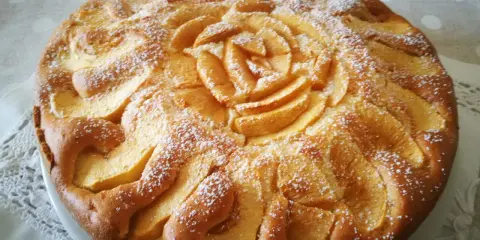 Deliziosa torta di mele senza glutine, decorata con fettine di mela disposte a rosa al centro e petali tutt'intorno, spolverata di zucchero a velo.