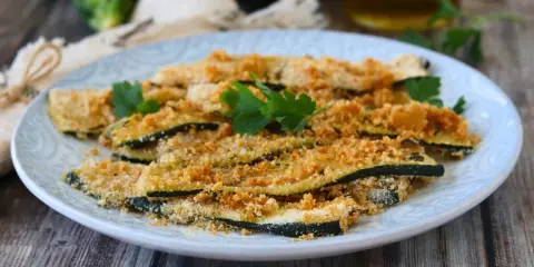 Fette di zucchine al forno, impanate e dorate, guarnite con prezzemolo fresco. Un contorno leggero e gustoso.