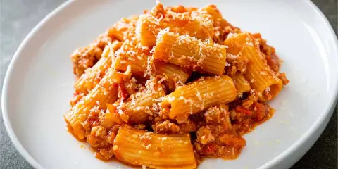 Piatto di rigatoni conditi con un ricco ragù, spolverati di parmigiano. La pasta alla zozzona ricetta perfetta per un pranzo gustoso.
