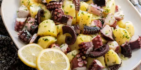 Un invitante polpo con patate, condito con prezzemolo e servito con spicchi di limone.