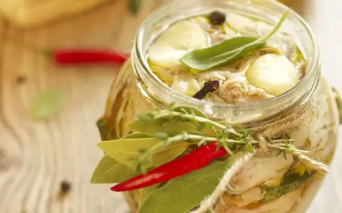 Tonno di coniglio in olio, con erbe aromatiche, peperoncino e spezie, in un barattolo di vetro decorato con spago.