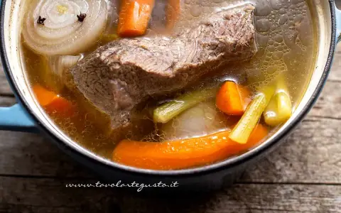 Un pezzo di carne succulenta cuoce lentamente in un brodo di carne ricco, con carote, sedano e cipolla.