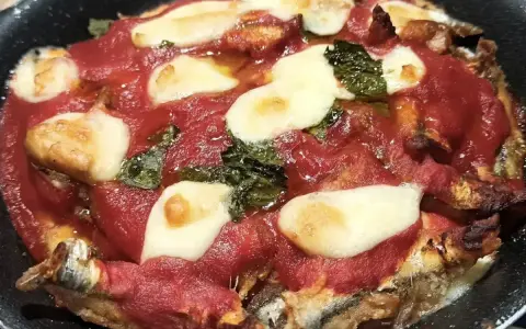 Parmigiana di alici in teglia, con pomodoro, mozzarella filante e basilico. Un piatto saporito e invitante.
