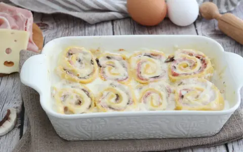 Rotolini di pasta con prosciutto e formaggio, cotti in una cremosa besciamella, sembrano piccoli nidi di rondine pronti per essere gustati.
