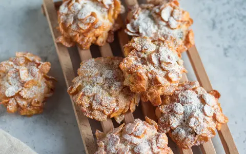 Deliziose rose del deserto, dolcetti croccanti ricoperti di fiocchi di mais e spolverati di zucchero a velo, su un tagliere di legno.
