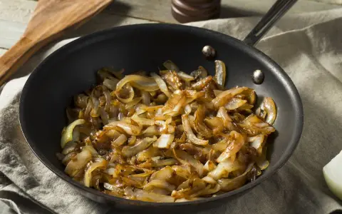 Cipolle caramellate in padella, pronte per insaporire un piatto. Un cucchiaio di legno attende accanto.