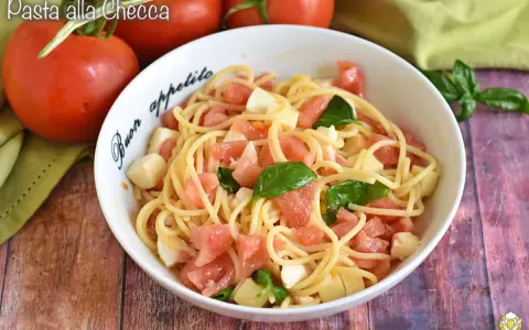 Un piatto di pasta alla checca con pomodori freschi, mozzarella e basilico, pronto per essere gustato.