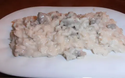 Un cremoso risotto con salsiccia, servito su un piatto bianco.