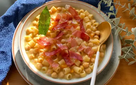 Un piatto fumante di pasta e ceci, guarnito con prosciutto crudo e una foglia di alloro.