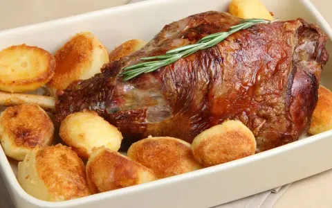 Un succulento agnello al forno con patate arrosto dorate, guarnito con un rametto di rosmarino fresco.