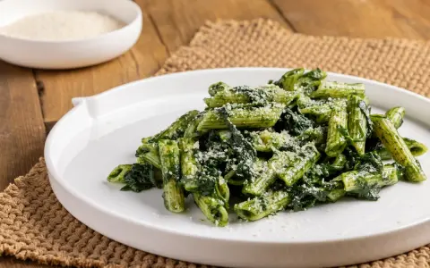 Piatto di pasta con spinaci e parmigiano grattugiato, servito su un piatto bianco.