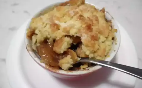 Un delizioso crumble di mele appena sfornato, con la sua crosta dorata e il ripieno succoso, pronto per essere gustato con un cucchiaino.