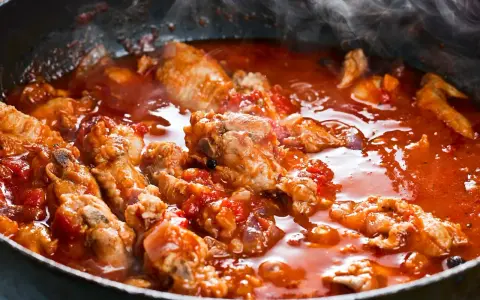Carne alla pizzaiola morbida che sobbolle in padella, con pomodoro e profumi invitanti.