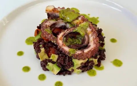 Delizioso polpo alla griglia su letto di riso venere, avocado e pomodorini, condito con salsa verde.