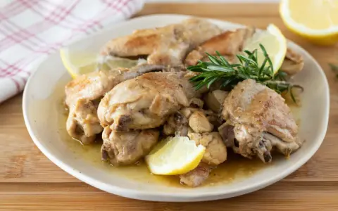 Succulento pollo al limone, dorato e profumato, servito con spicchi di limone fresco e rosmarino su un piatto bianco.