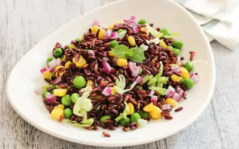 Insalata di riso Venere colorata con piselli, mais, cipolla rossa e lattuga croccante, guarnita con menta fresca.