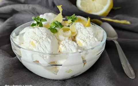 Coppa di cremoso gelato al limone, guarnita con scorzette e foglioline di menta. Un limone fresco sullo sfondo.