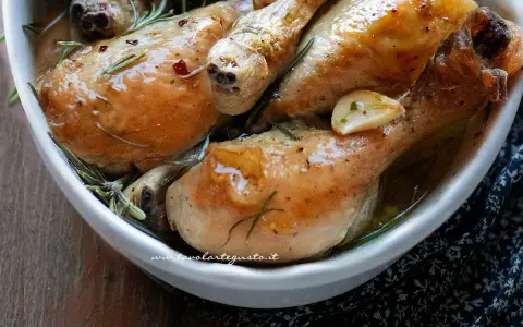 Cosce di pollo succulente, dorate e profumate al rosmarino e aglio, servite in una ciotola bianca.