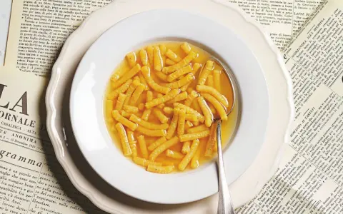 Passatelli in brodo, un classico della ricetta italiana, serviti in un piatto bianco su vecchie pagine di giornale.