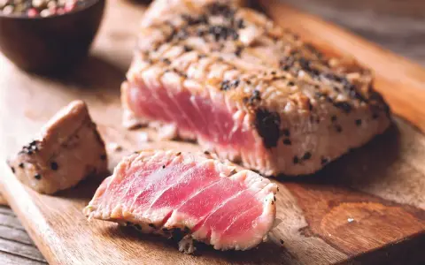 Trancio di tonno scottato, con crosta di pepe nero, servito su tagliere di legno.