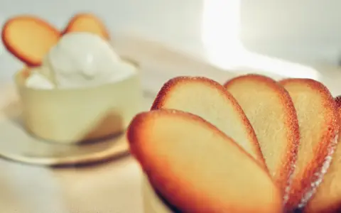 Biscotti croccanti a forma di lingue di gatto, alcuni in primo piano, altri decorano una coppa di panna montata.