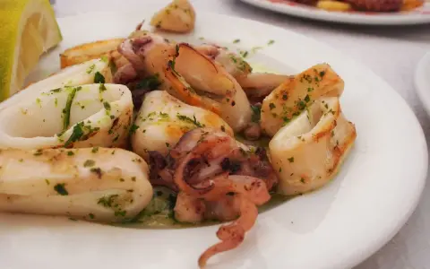 Calamari in padella, succulenti e dorati, conditi con prezzemolo fresco e serviti con una fetta di limone.