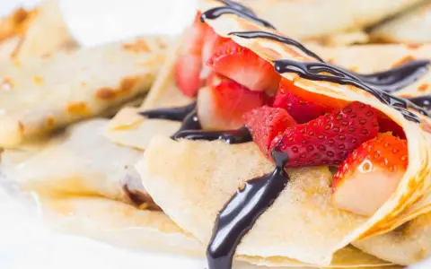Deliziose crepes senza burro, ripiene di fragole fresche e ricoperte da una cascata di cioccolato fondente.