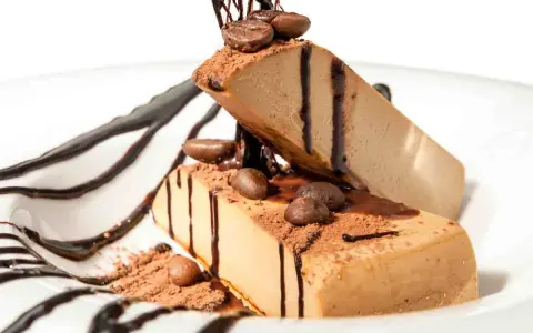 Due fette di semifreddo al caffè, decorate con cacao, chicchi di caffè e salsa al cioccolato, su un piatto bianco.