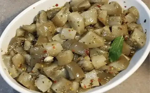 Un invitante piatto di insalata di melanzane, condita con olio, aglio e peperoncino, guarnita con una fogliolina di menta.