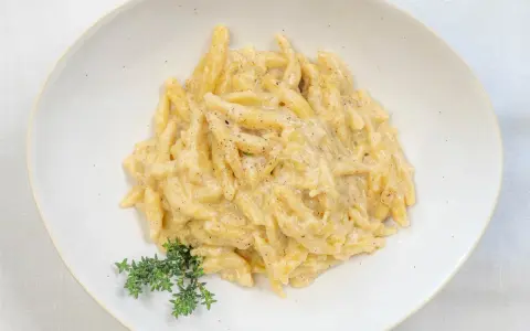 Ravioles val Varaita, pasta fresca condita con una cremosa salsa al formaggio e pepe nero, guarnita con timo fresco.