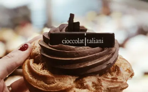 Una mano con smalto rosso tiene un delizioso dolce al cioccolato, decorato con la scritta "cioccolatitaliani".