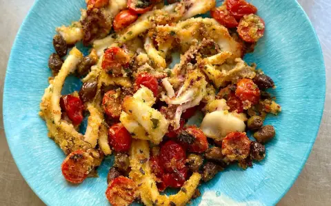 Calamari gratinati al forno su piatto blu, con pomodorini e olive. Croccanti e saporiti, un piatto che profuma di mare.