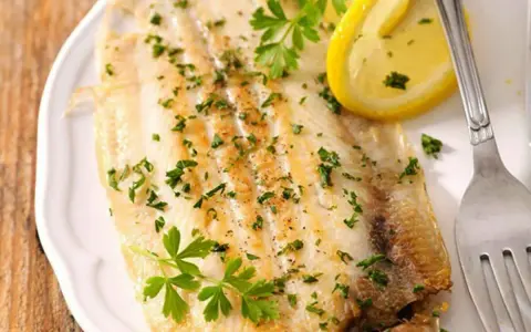 Sogliola al forno, dorata e profumata, guarnita con prezzemolo fresco e spicchi di limone. Un piatto leggero e saporito.