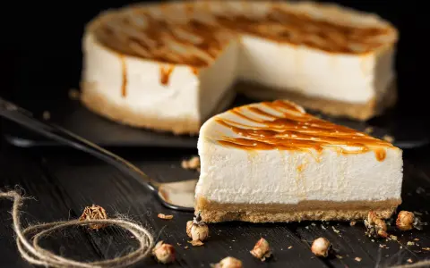 Una fetta di cheesecake senza gelatina, con colatura di caramello, su un piatto scuro.