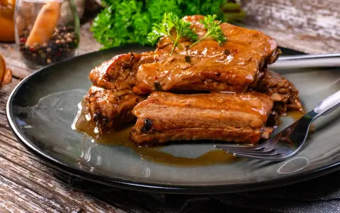 Succulente costine di maiale glassate, guarnite con prezzemolo fresco, servite su un piatto scuro con una forchetta.