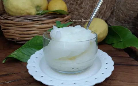 Granita al limone fatta in casa, fresca e dissetante, servita in una coppetta con foglioline di menta. Limoni freschi in un cesto sullo sfondo.