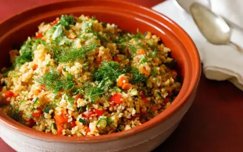Tabulè di verdure fresco e colorato, con pomodori, zucchine e erbe aromatiche, servito in una ciotola di terracotta.