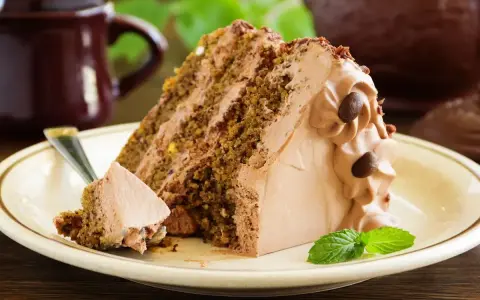 Una fetta di torta al cioccolato con abbondante crema al latte, guarnita con chicchi di caffè e una fogliolina di menta.