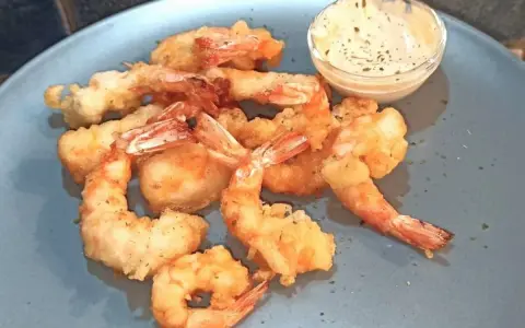 Gamberi in tempura dorati e croccanti, serviti su un piatto blu con una ciotolina di salsa cremosa.