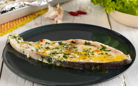 Un succulento pesce spada al forno, condito con erbe aromatiche e olio d'oliva, servito su un piatto scuro.
