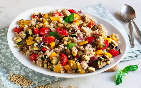 Un piatto colorato di insalata di grano saraceno con verdure miste arrosto: peperoni, zucchine, melanzane e pomodorini.