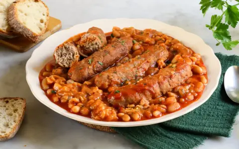 Piatto di salsiccia e fagioli in umido, servito con pane tostato.