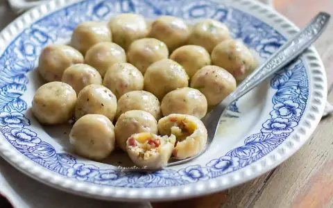 Gnocchi di pane su piatto decorato, uno spezzato rivela un ripieno saporito.