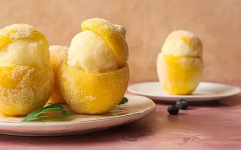 Sorbetto al limone senza albume servito in scorze di limone ghiacciate, guarnito con foglioline di menta e mirtilli.