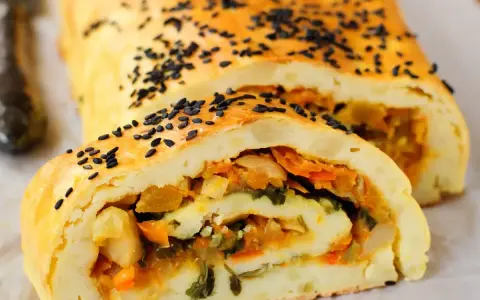 Rotolo di patate dorato, cosparso di semi neri, con un ripieno colorato di verdure.